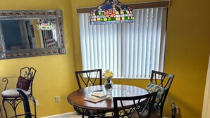A dining area with a round table, chairs, a vase with flowers, a vacuum cleaner, and a mirror on the wall.