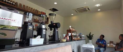 Un interior de cafetería con mostrador, máquinas de café y asientos.