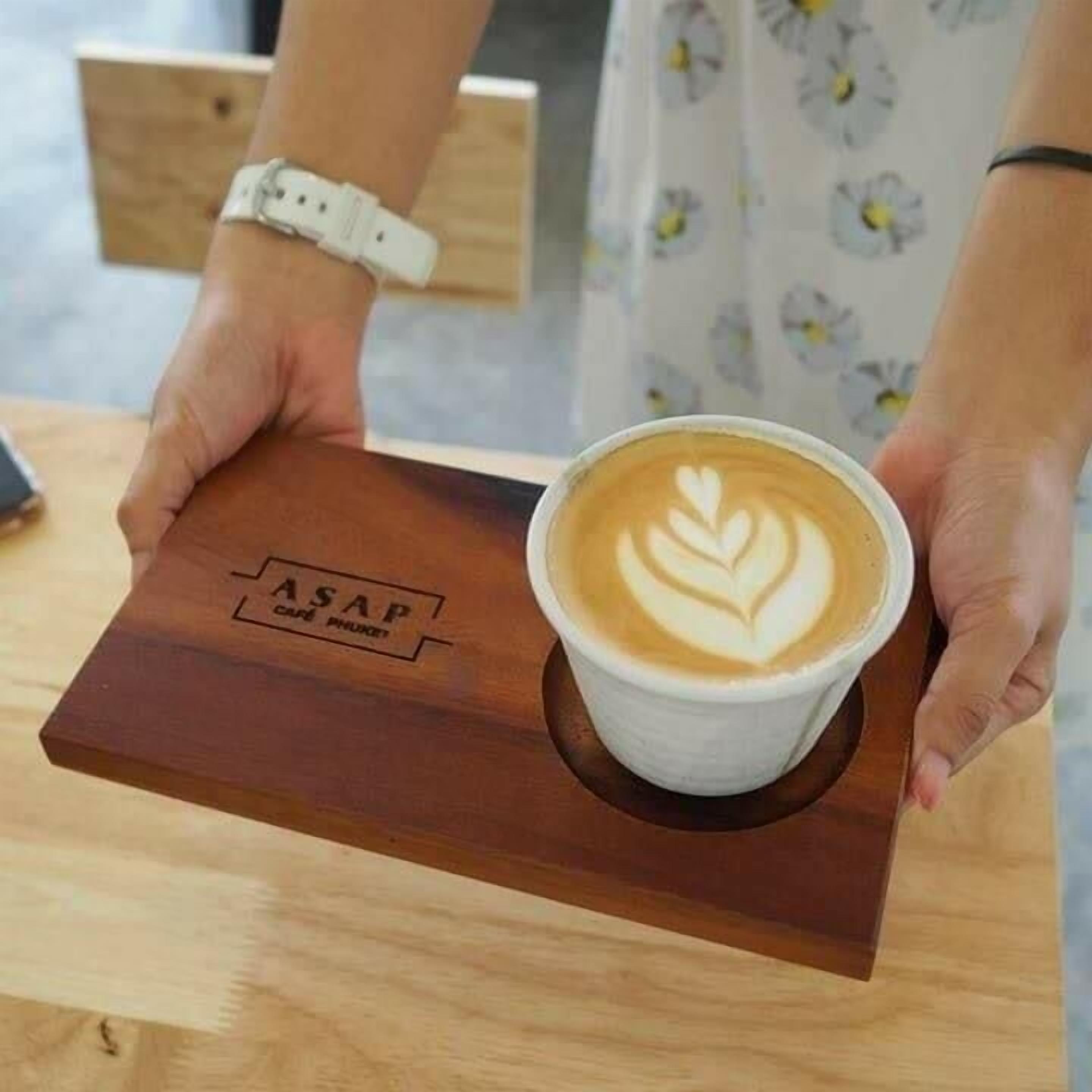 A person holding a cup of coffee with latte art on a wooden tray.