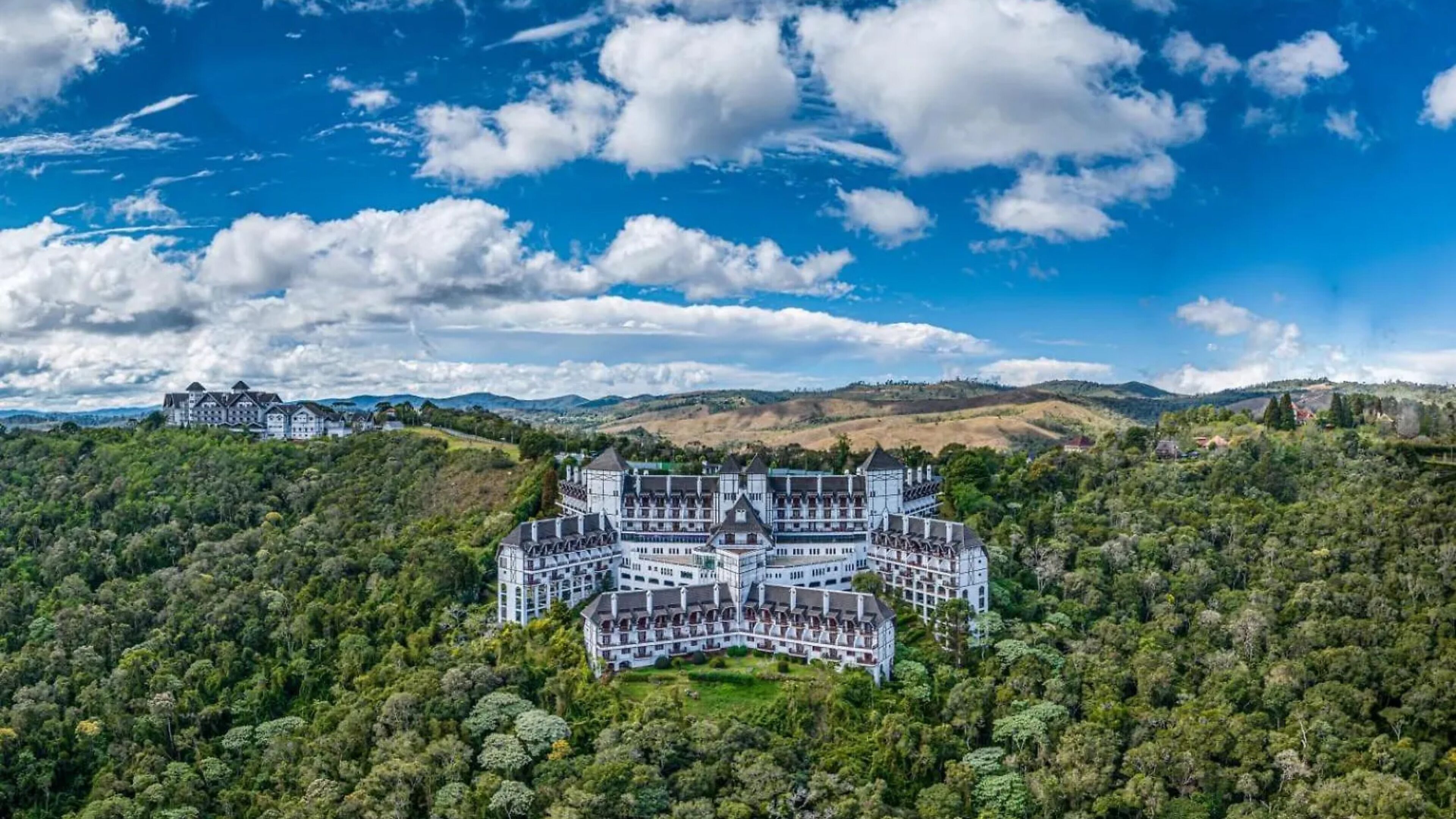 A large, castle-like hotel with multiple wings and a lush, forested landscape in the background.