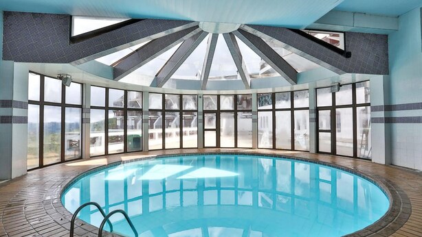 A large indoor swimming pool with a clear view of the surrounding landscape through large windows. - Duplex em Castelo Piscina e Lareira (Campos do Jordão)