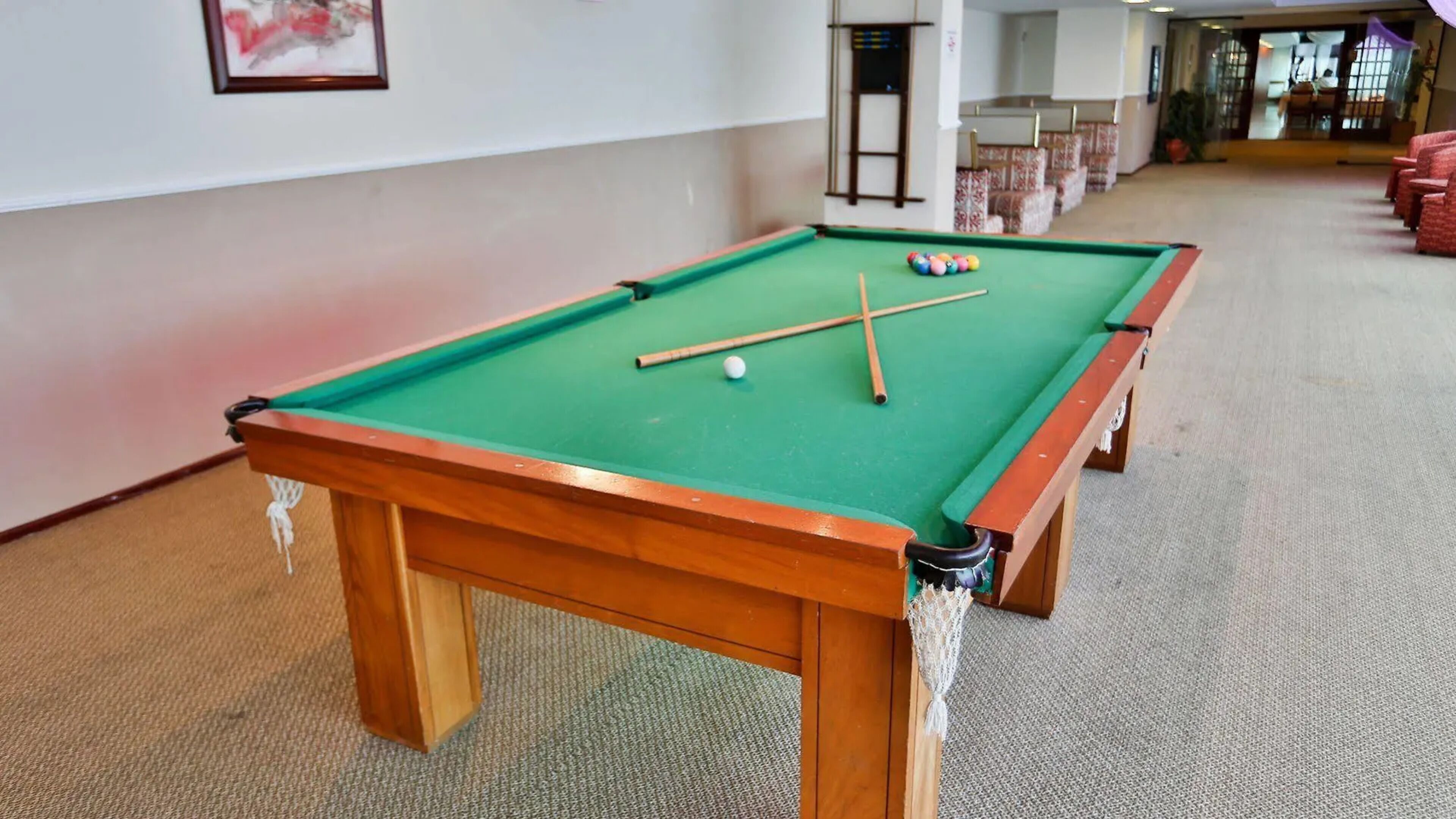 Une table de billard recouverte d’un drap vert, dotée d’un cadre en bois et comprenant deux queues de billard.