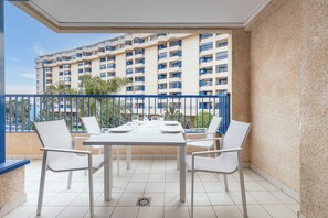 Un balcon avec une table et des chaises blanches, une rambarde bleue et une vue sur un immeuble de grande hauteur doté de nombreux balcons.