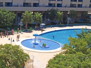 A swimming pool with a water slide, palm trees, and a building in the background.