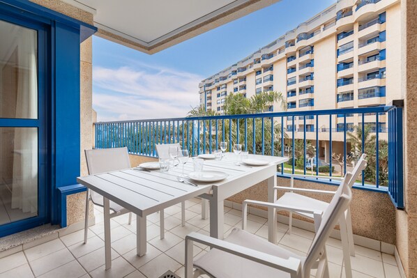 A balcony with a white table set for dining, blue railings, and a view of a high-rise building.