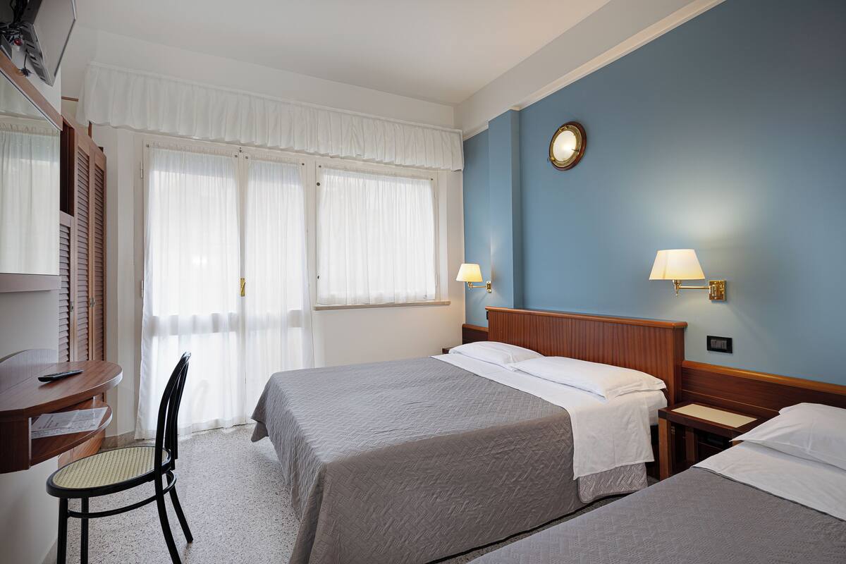 Una habitació d'hotel amb dos llits, un escriptori, una cadira i una finestra amb cortines.