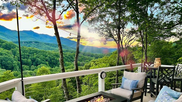 Eine Terrasse mit Sitzgelegenheit im Freien, einer Feuerstelle und Blick auf eine bewaldete Berglandschaft.