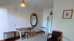 Ein Zimmer mit Schreibtisch aus Holz, zwei Stühlen, einem Spiegel, einem Regal und einer Pendelleuchte.
