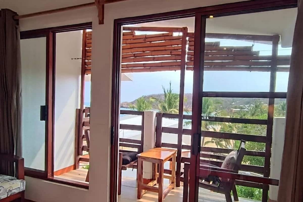 Una stanza con una porta scorrevole in vetro che si apre su uno spazio esterno con una pergola in legno, un tavolo e una sedia.