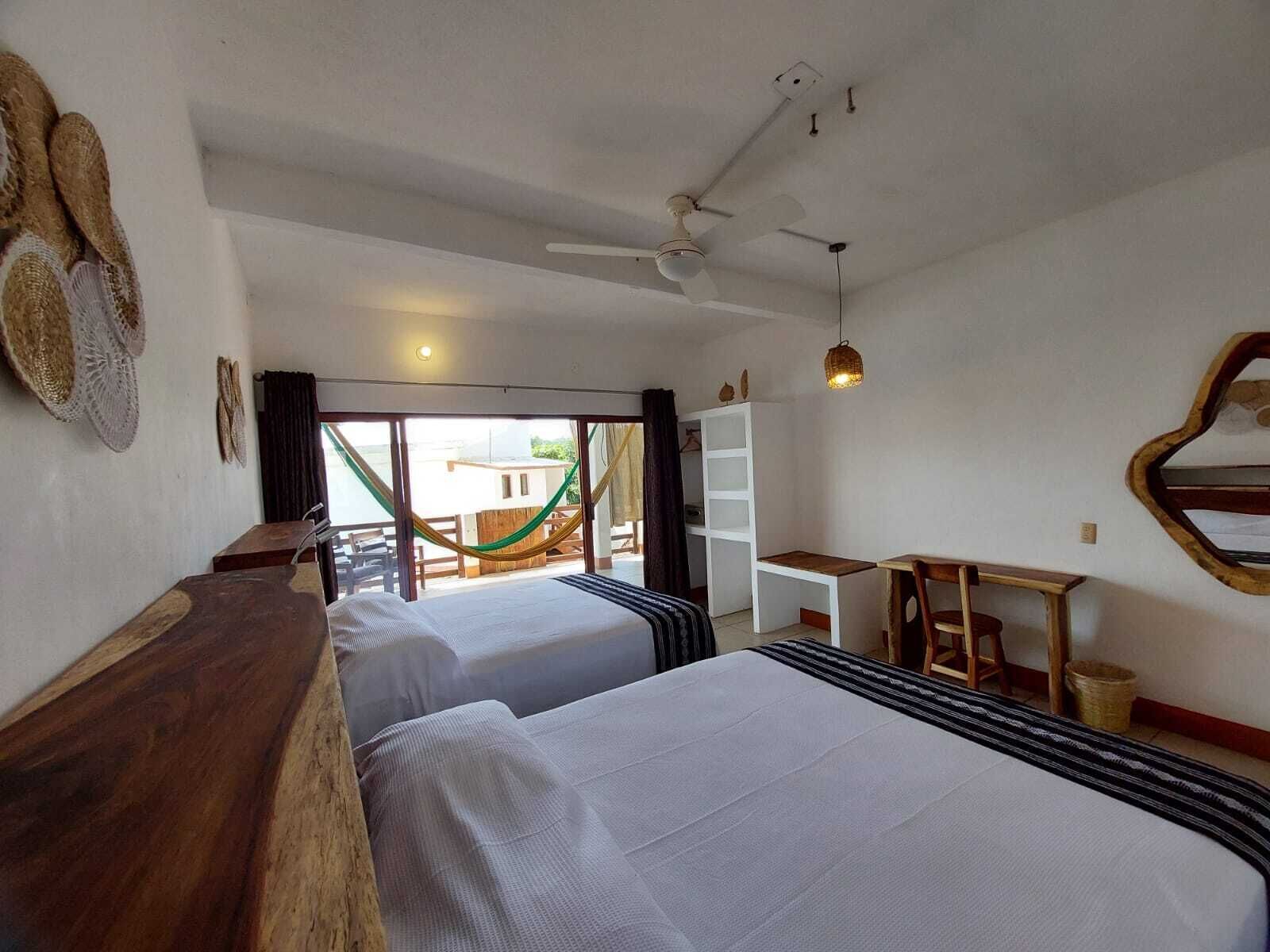 Une chambre avec deux lits, un bureau, une chaise, un luminaire suspendu et une vue sur l’extérieur.