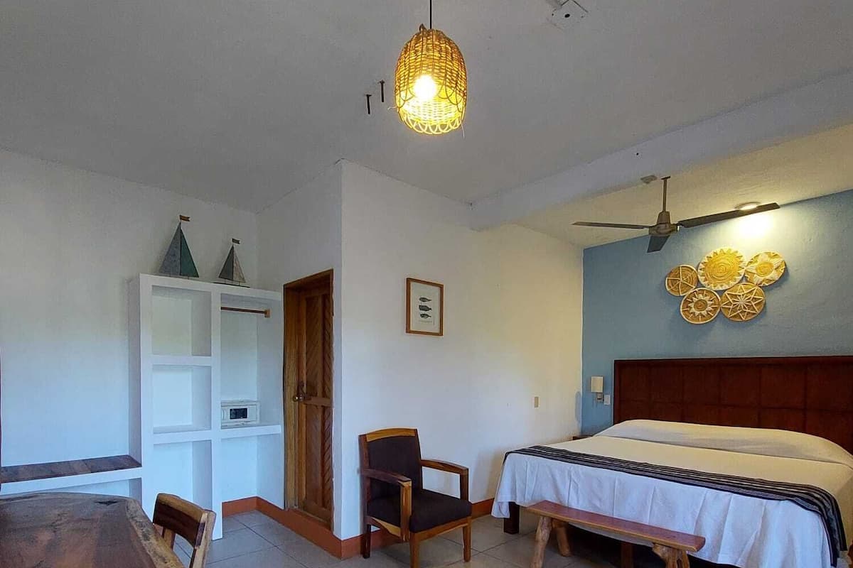 Una camera da letto con un letto, una scrivania e una sedia. Presente una ventola a soffitto e un lampadario.