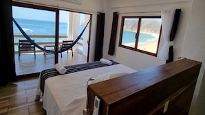 Ein Schlafzimmer mit einem Bett, einem Nachttisch aus Holz, einem Deckenventilator und Blick auf den Ozean.