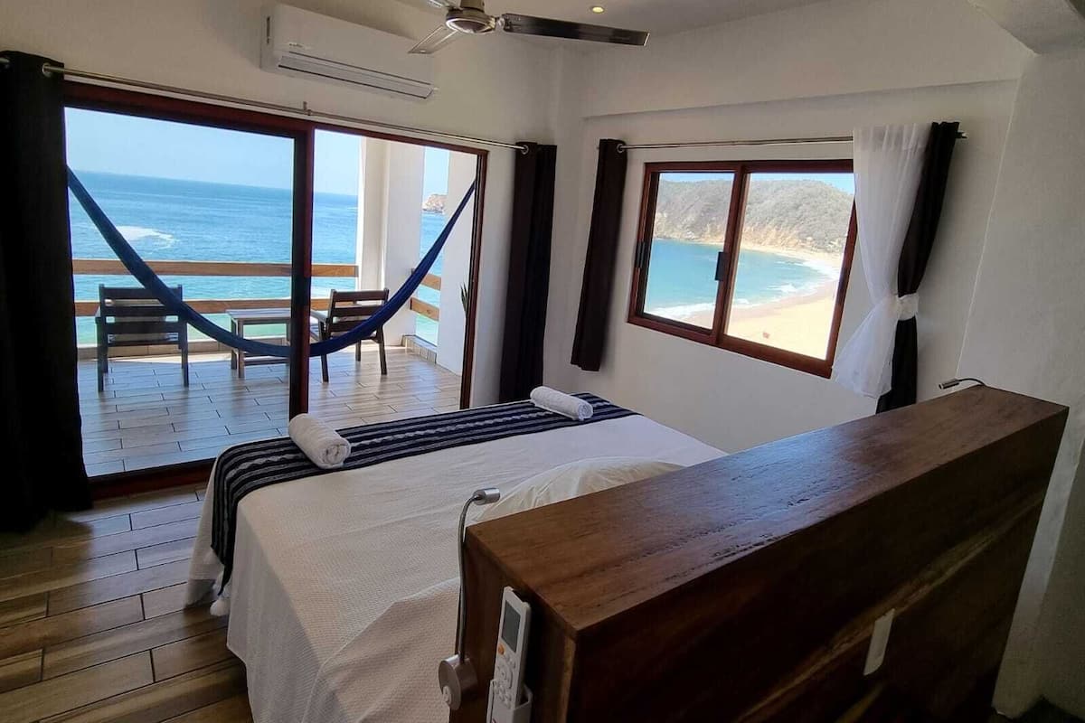 Una camera da letto con un letto, un comodino in legno, una ventola a soffitto e vista sull'oceano.