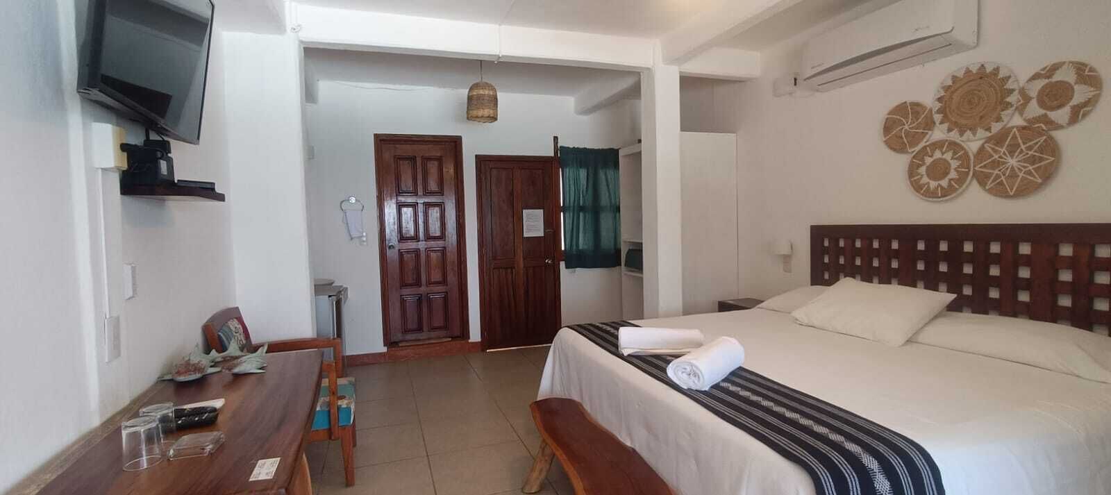A hotel room with a bed, a desk with a chair, a television, and a door leading to another room.