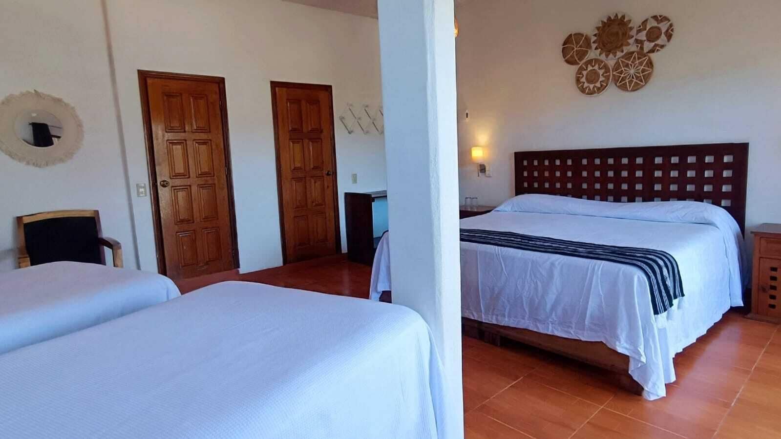 A hotel room with two single beds, a wooden headboard, a wall-mounted light fixture, and a door with a mirror.