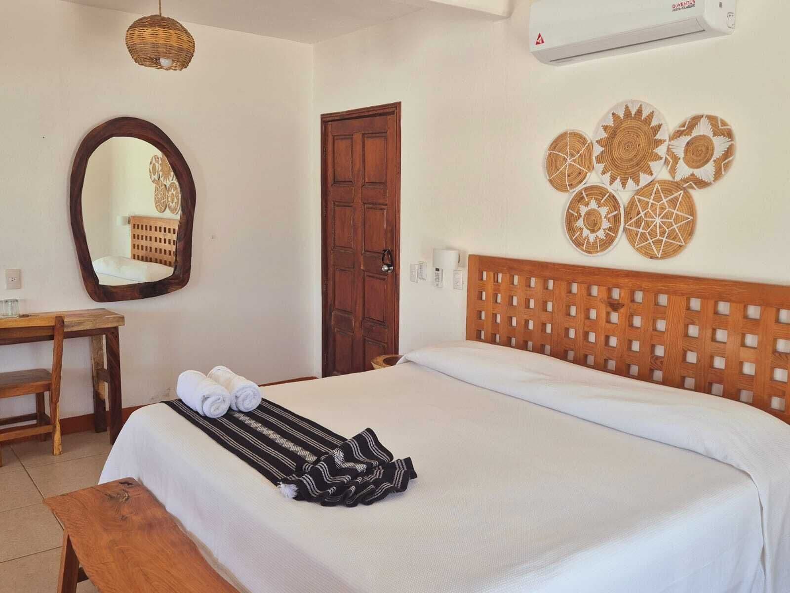 A neatly made bed with a striped blanket, a wooden headboard, and a wall-mounted mirror.