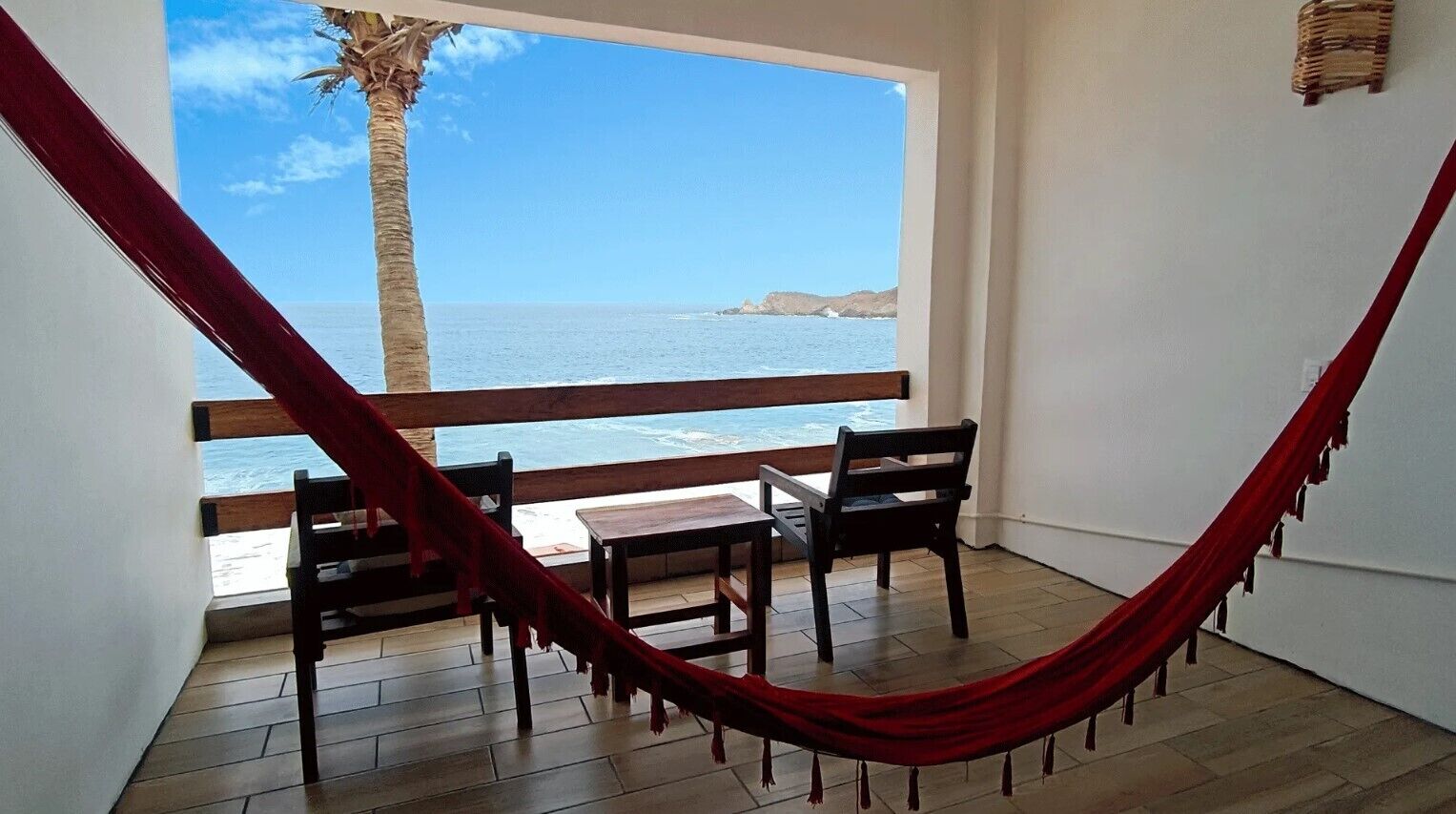 A balcony with a red hammock, wooden chairs, and a view of the ocean.