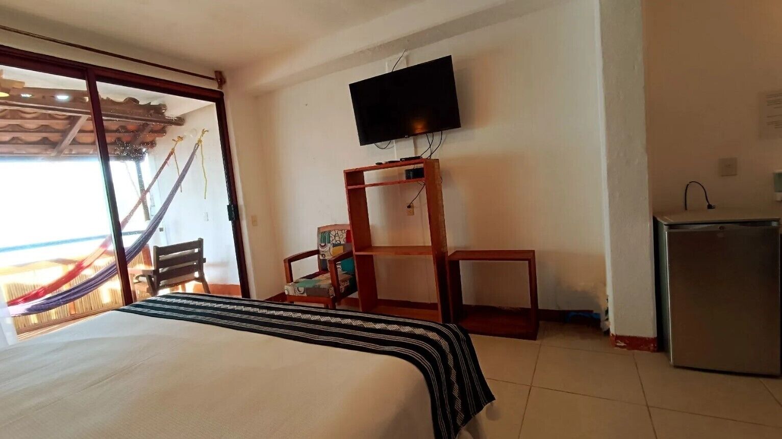 A hotel room with a bed, a television mounted on the wall, a small table, a chair, and a refrigerator.