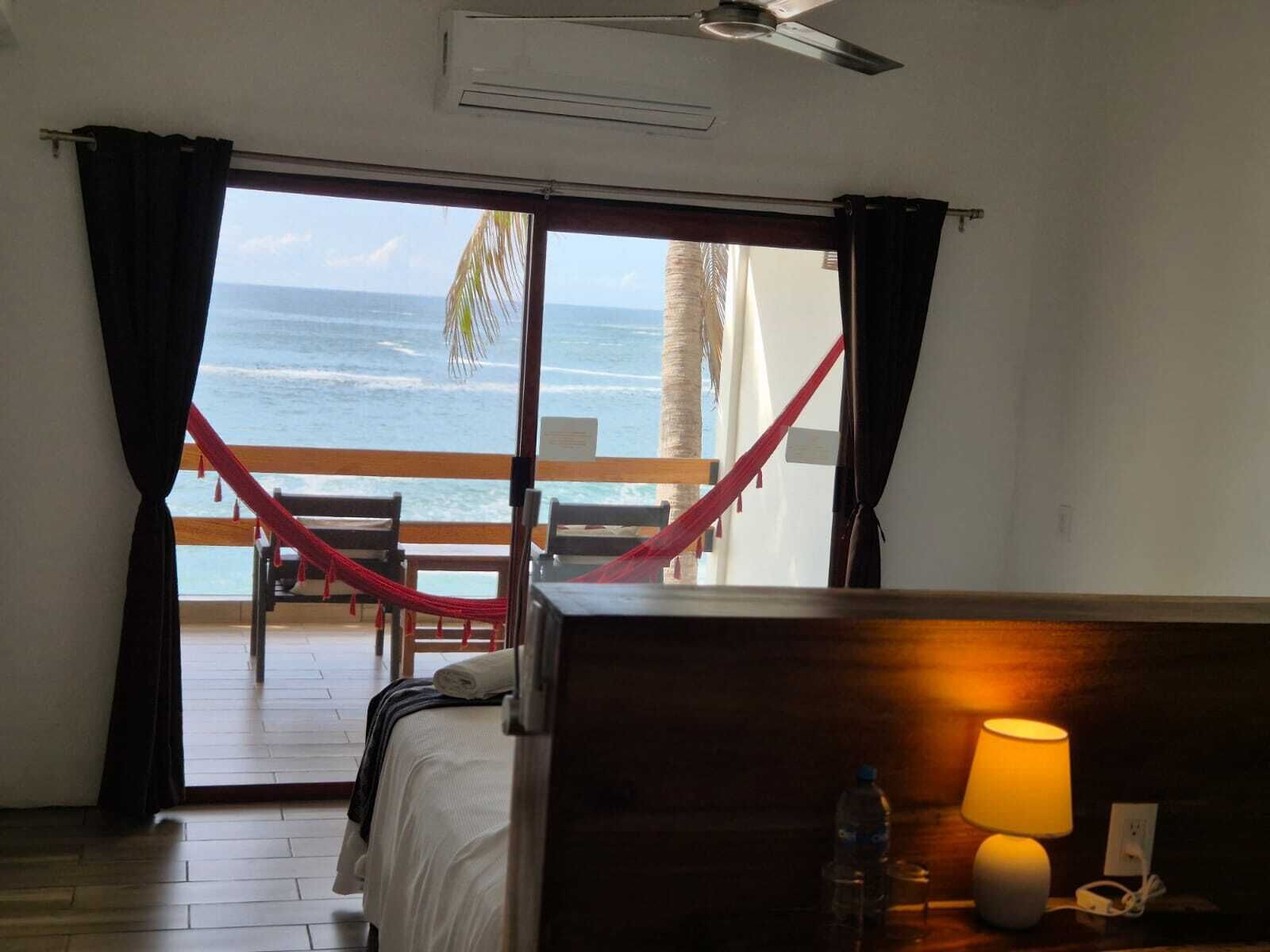 A room with a bed, a desk with a lamp, a water bottle, and a view of the ocean through a sliding door.