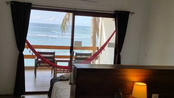 A room with a bed, a desk with a lamp, a water bottle, and a view of the ocean through a sliding door.