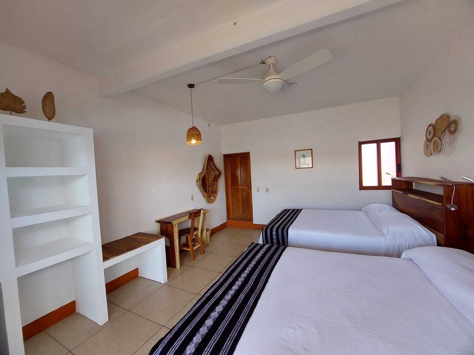 A bedroom with two beds, a desk, a chair, a wardrobe, and a ceiling fan.