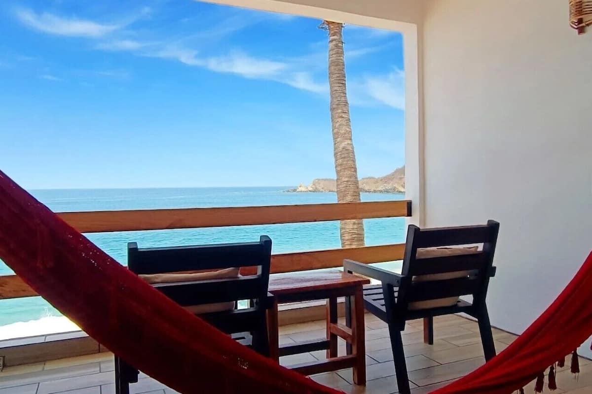 Un balcone con vista sul mare, due sedie e un'amaca rossa.
