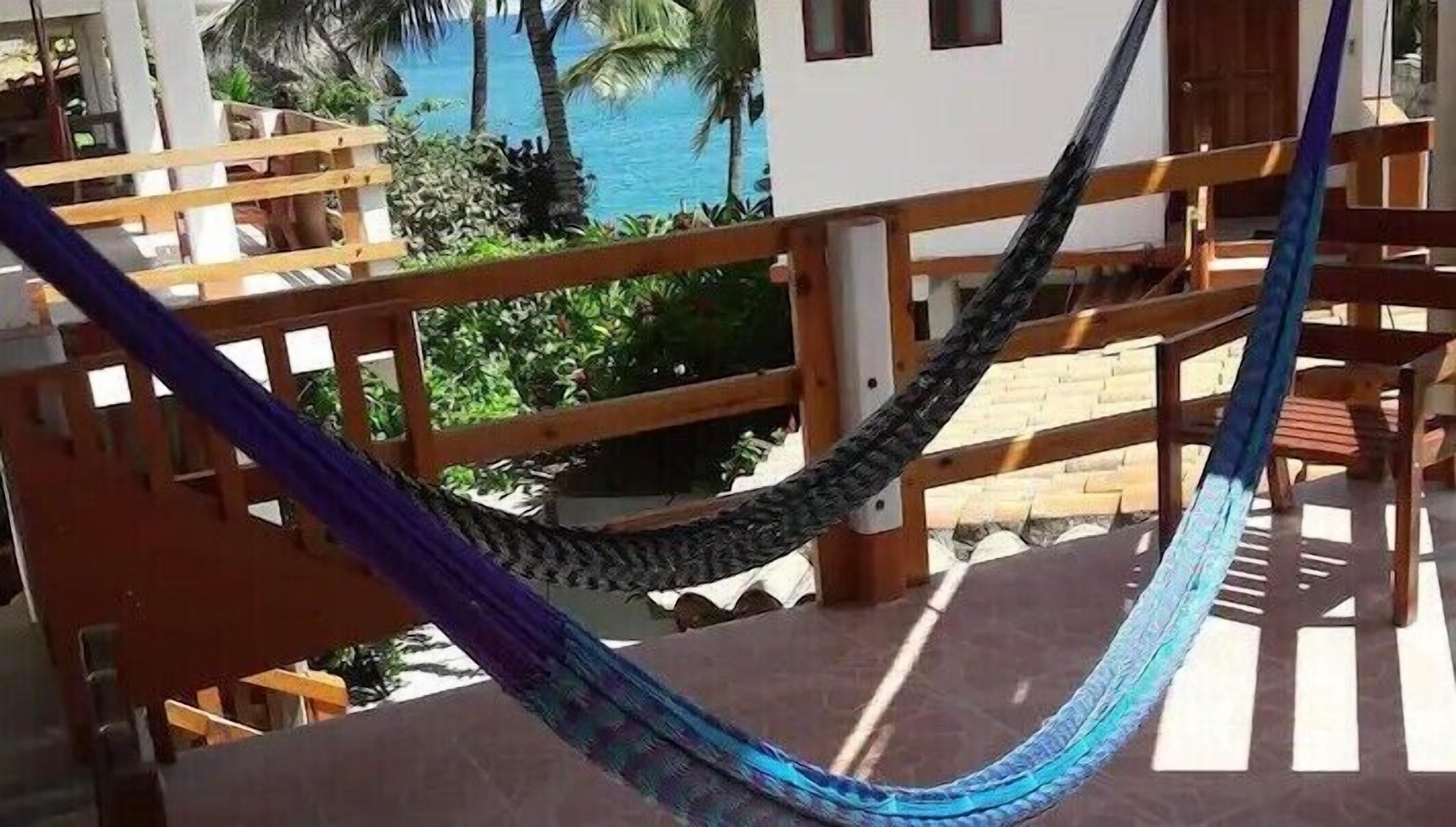 A hammock on a balcony with a view of the ocean and palm trees.