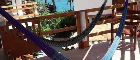 A hammock on a balcony with a view of the ocean and palm trees.