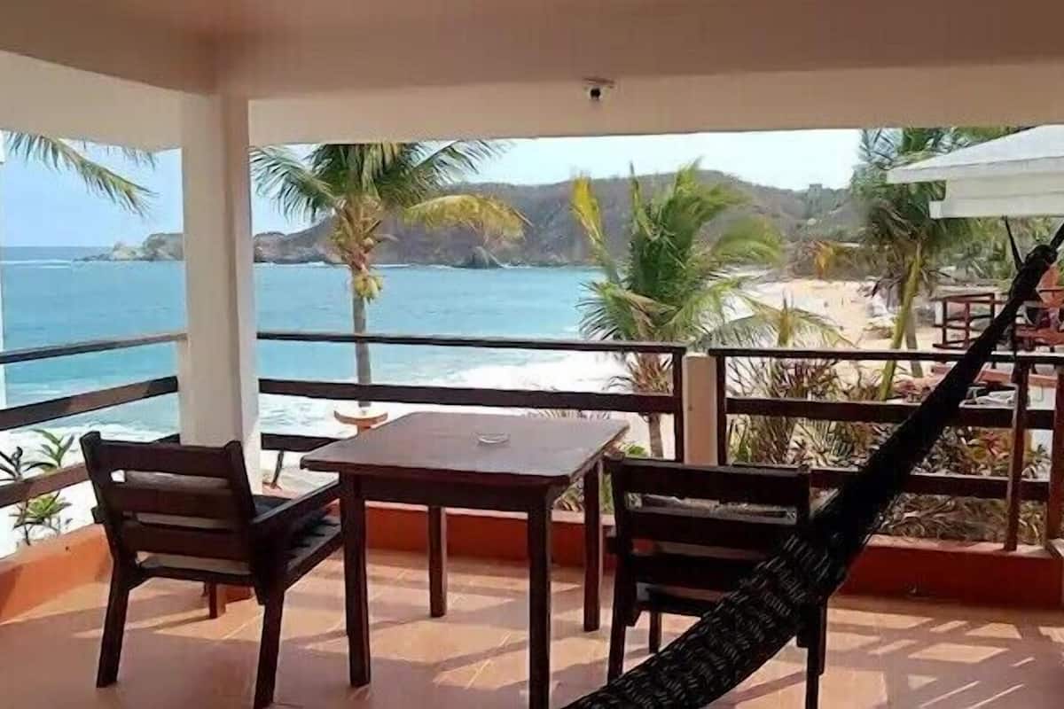Un balcone con vista sulla spiaggia, un'amaca e un tavolo con sedie.