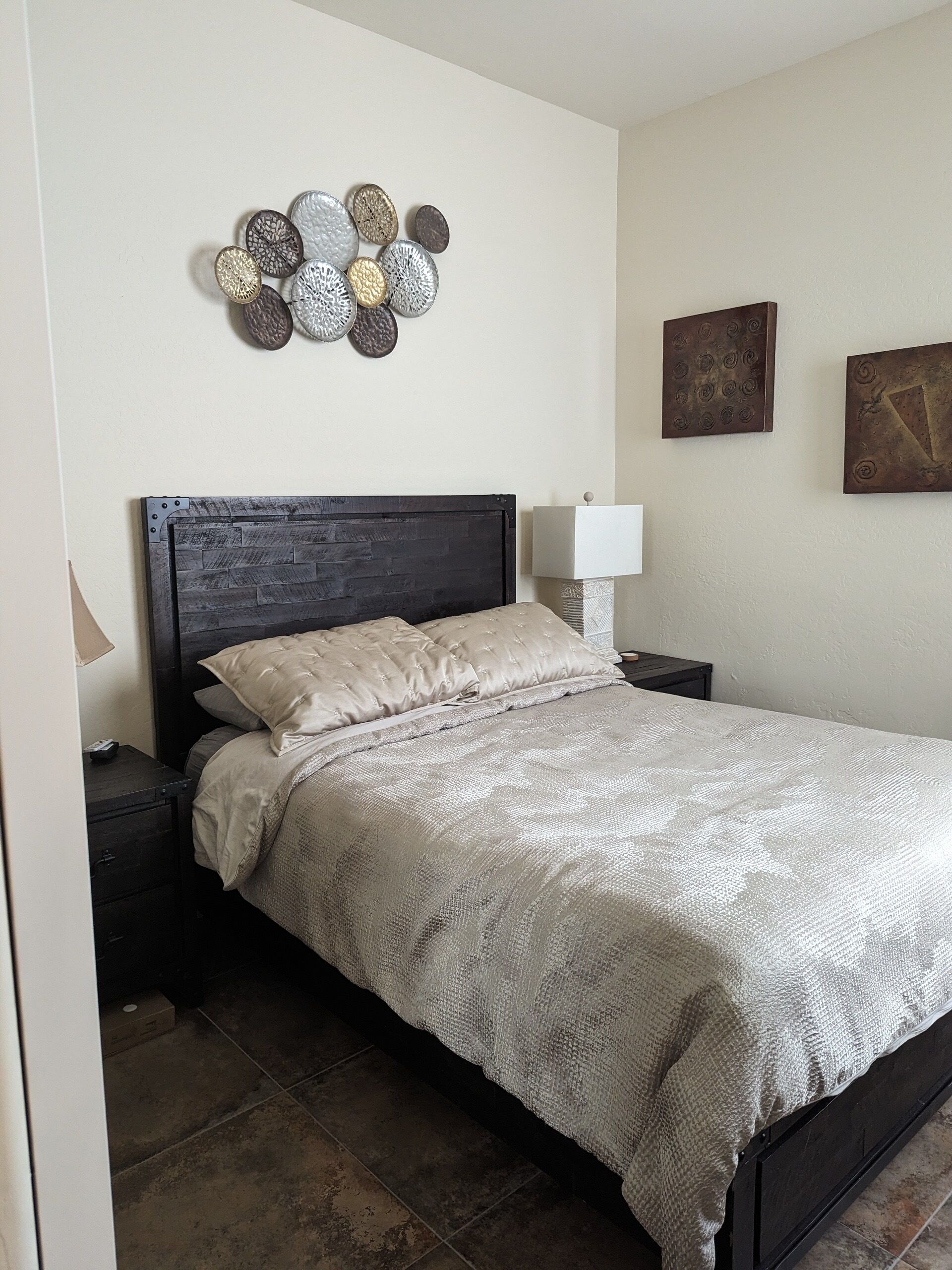 Un dormitorio con un cabecero de madera oscura, una colcha acolchada color beige y un adorno en la pared sobre la cama.