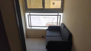 Una habitació petita amb finestra, un sofà i un terra amb rajoles.