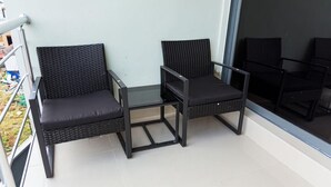 Dos sillones de mimbre negro con cojines en un balcón con baranda de cristal.