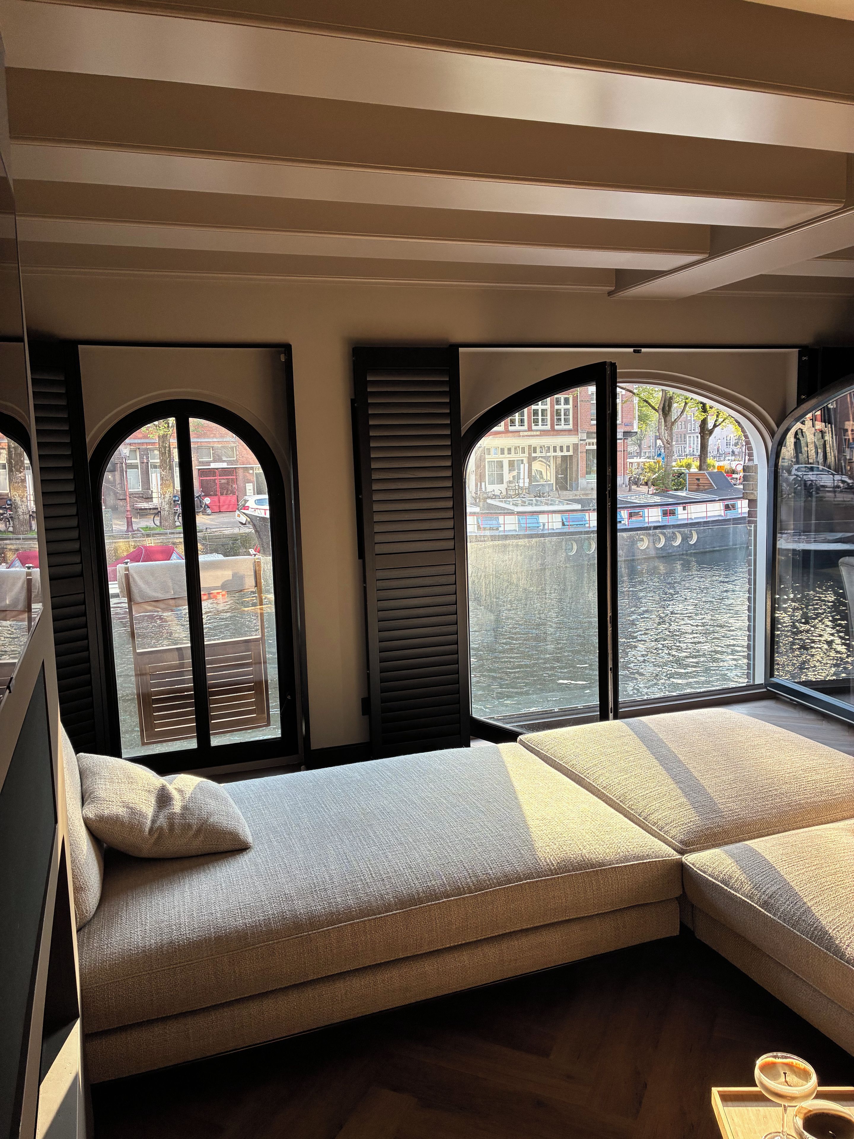 A room with a large window overlooking a canal, a sofa, and a wooden floor.
