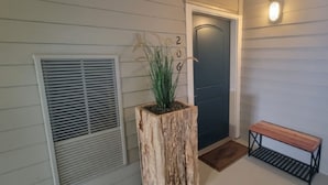 A wooden planter with a plant, a door with a number, and a bench.