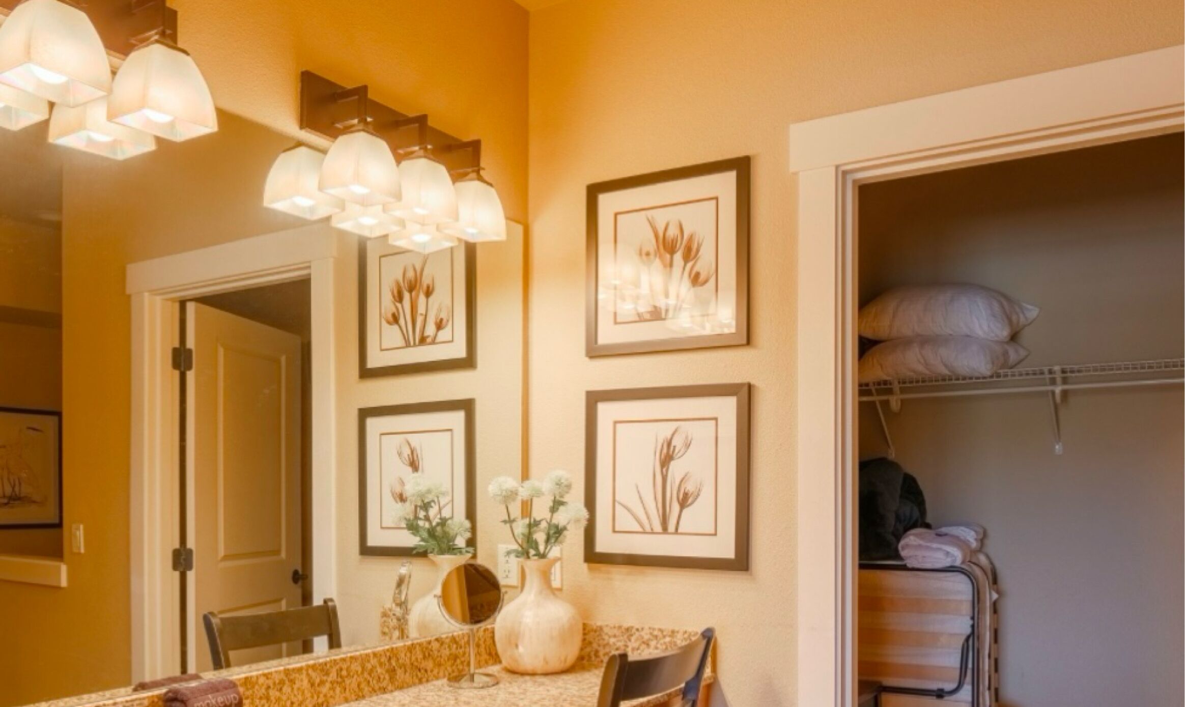 A dining area with a table, chairs, and a vase of flowers. There are framed botanical prints on the wall.