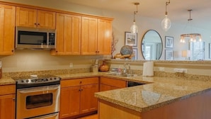 A kitchen with wooden cabinets, stainless steel appliances, granite countertops, and pendant lighting.