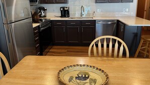 Une cuisine moderne avec des meubles de rangement en bois foncé, des appareils électroménagers en acier inoxydable et une table à manger en bois agrémentée d’un saladier décoratif.