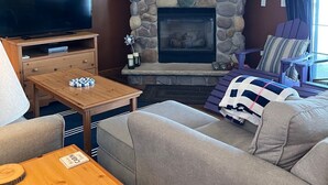 Un salon chaleureux avec une cheminée en pierre, un téléviseur à écran plat, une table basse en bois et des sièges confortables.