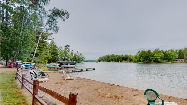 Une zone au bord du lac, avec une plage de sable, une terrasse en bois et un quai où sont amarrés des bateaux.