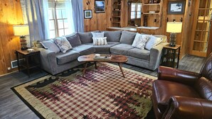 Ein gemütliches Wohnzimmer mit einem grauen Ecksofa, einem Couchtisch und einem gemusterten Teppich.