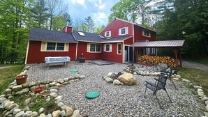 Ein rotes Haus mit einer Laube, einer Kiesterrasse und einem Holzstapel.