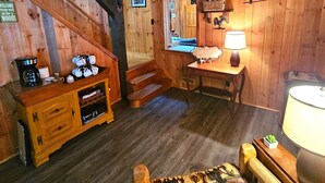 Ein gemütliches Blockhaus-Interieur mit einer Holztreppe, einem Schreibtisch mit Lampe und einer Kaffeestation.