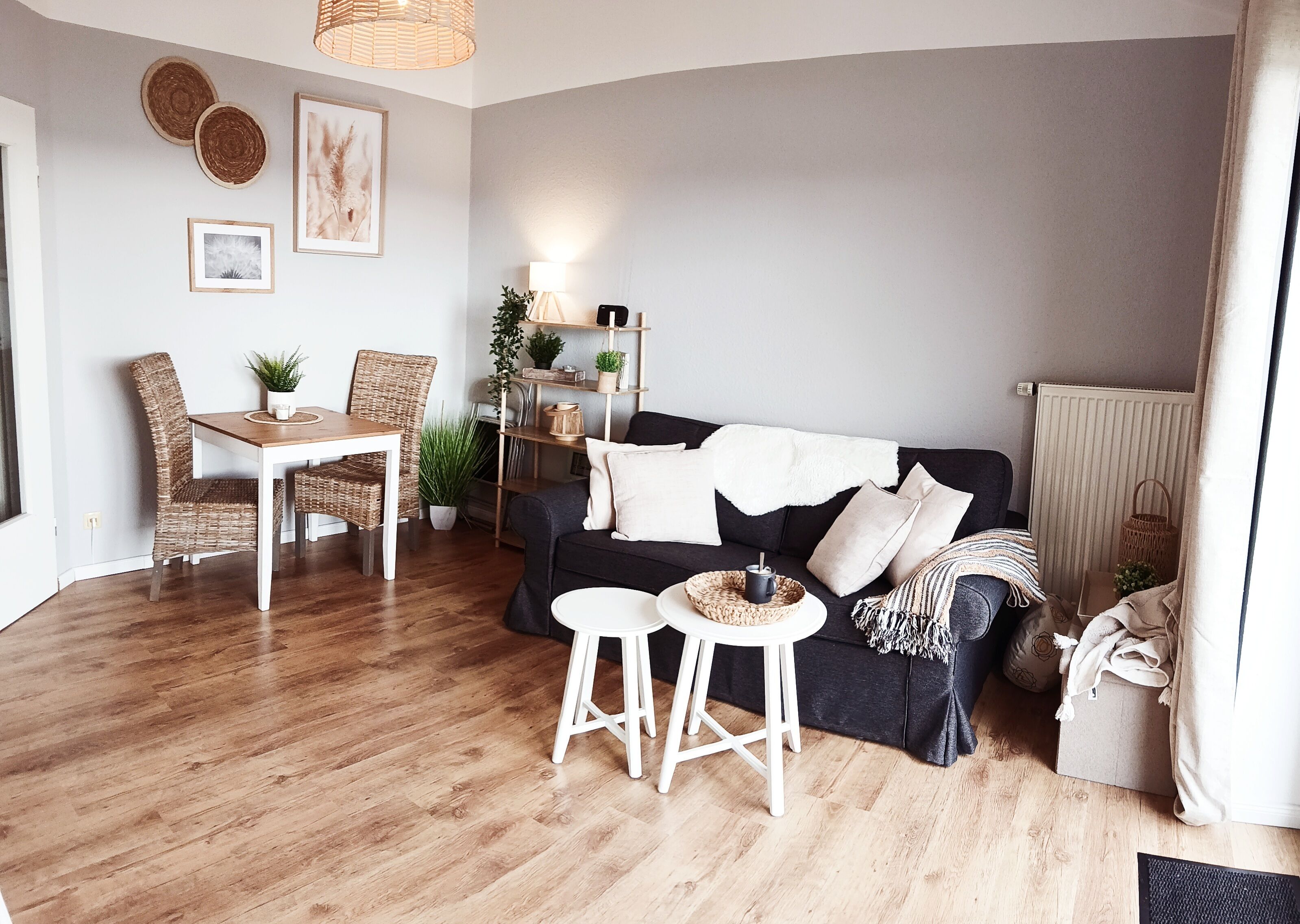 Ein Wohnzimmer mit einem dunklen Sofa, einem weißen Couchtisch, Korbstühlen, einem Holzesstisch und einem kleinen Beistelltisch.