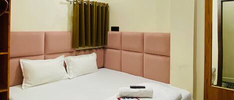 A neatly made bed with white linens and pillows, a ceiling fan, a window with curtains, and a wooden headboard.