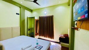 A hotel room with a bed, a television mounted on the wall, a ceiling fan, and a window with curtains.