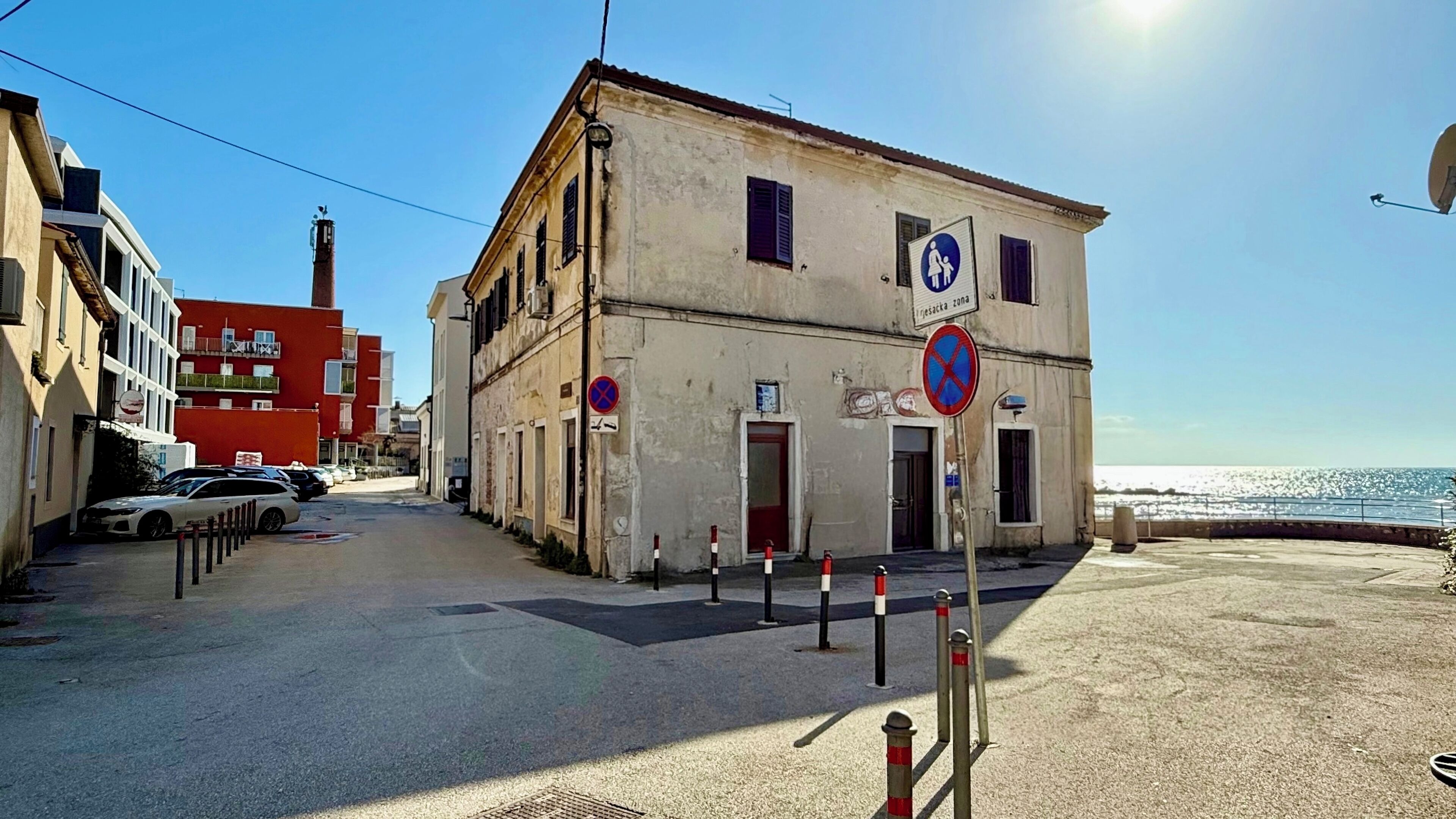 A coastal street with a building featuring a pedestrian zone sign and a no parking sign.