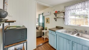 Une cuisine de taille réduite, équipée d’un évier, d’une petite table et d’une fenêtre agrémentée de rideaux à motifs.