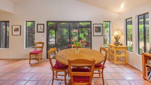 Un comedor con una mesa redonda de madera, cuatro sillas de madera con cojines rojos, una mesita auxiliar de madera con una lámpara y una estantería.