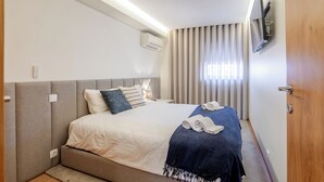 A bedroom with a bed, bedside tables, a TV, and a window with curtains. - Beachouse Pvz 🌊🌅 (Póvoa de Varzim)