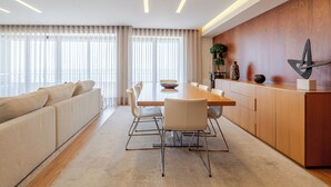 A modern living room with a sofa, dining table, chairs, and a kitchen area with wooden cabinets and a plant. - Beachouse Pvz 🌊🌅 (Póvoa de Varzim)